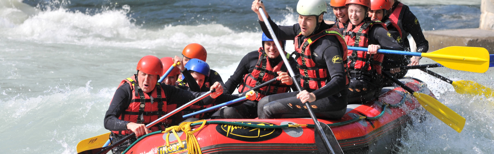Students are whitewater rafting. They are not looking at the camera and have excited expressions.
